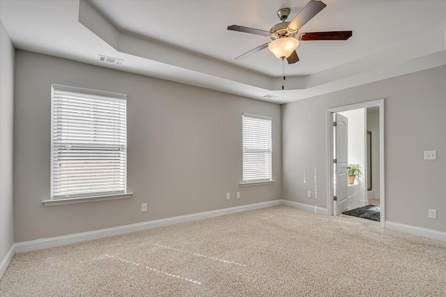 carpeted spare room with a tray ceiling, baseboards, visible vents, and ceiling fan