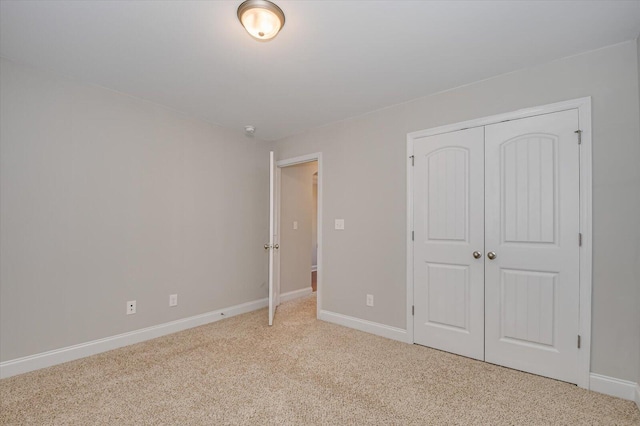 unfurnished bedroom featuring light colored carpet, a closet, and baseboards