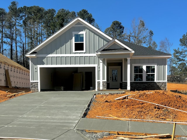 view of front of property with roof with shingles, concrete driveway, board and batten siding, a garage, and stone siding