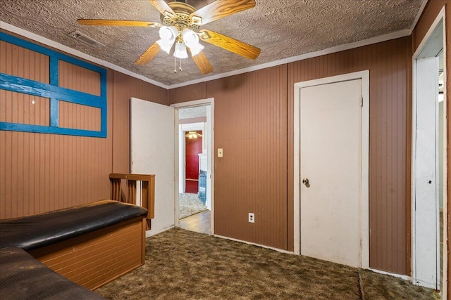 interior space featuring ceiling fan, ornamental molding, dark carpet, and a textured ceiling