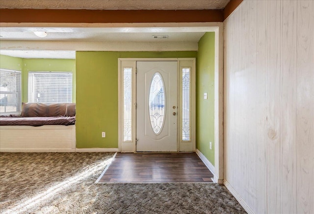 foyer entrance with a healthy amount of sunlight, dark carpet, and beamed ceiling