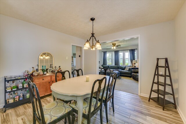 dining area featuring a textured ceiling, baseboards, light wood finished floors, and ceiling fan with notable chandelier