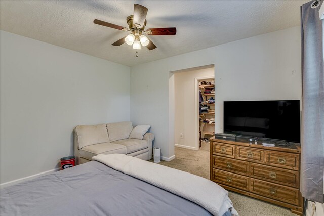 bedroom featuring ceiling fan, a textured ceiling, baseboards, a spacious closet, and carpet