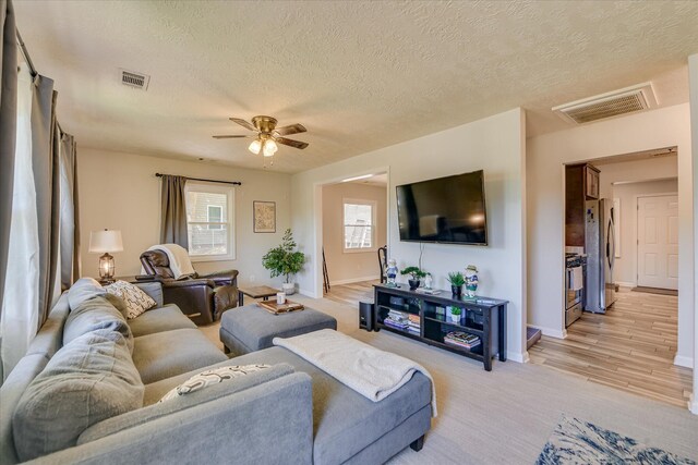 living room featuring baseboards, ceiling fan, a textured ceiling, and visible vents