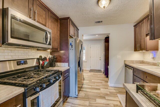 kitchen featuring backsplash, visible vents, appliances with stainless steel finishes, light wood-type flooring, and light countertops