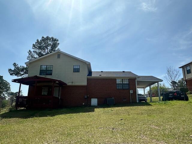 back of property featuring a lawn, a carport, central AC, and brick siding