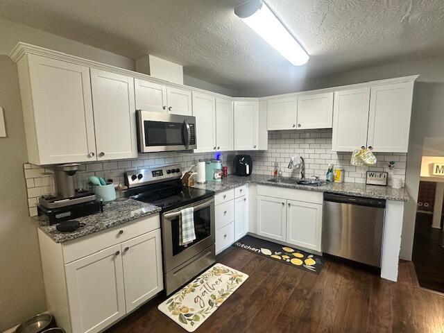 kitchen with dark wood-style flooring, a sink, light stone counters, white cabinets, and appliances with stainless steel finishes