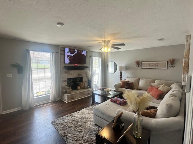living room with dark wood-type flooring, a fireplace, a healthy amount of sunlight, and a ceiling fan