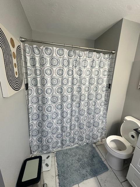 full bath featuring toilet, a shower with shower curtain, and a textured ceiling