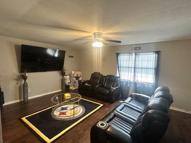 living room featuring a textured ceiling, baseboards, ceiling fan, and wood finished floors