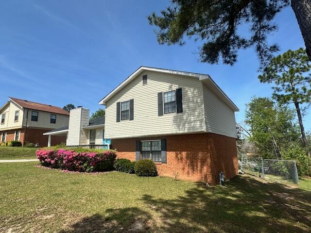 view of side of home featuring fence, brick siding, and a yard