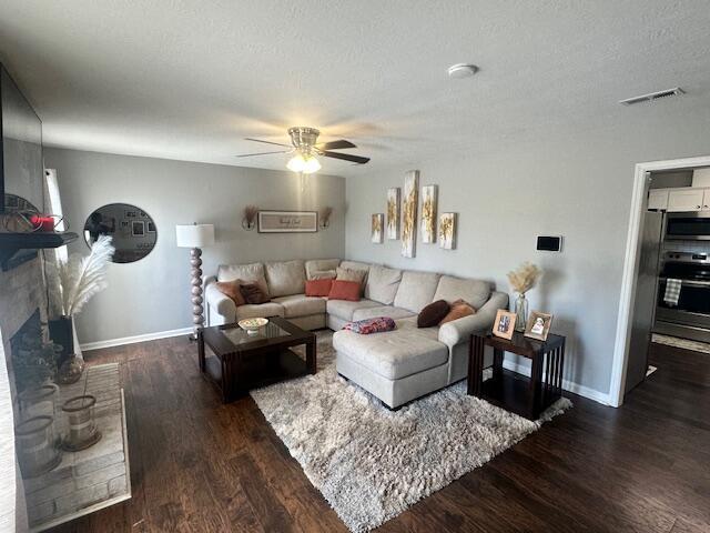 living room with a textured ceiling, visible vents, baseboards, ceiling fan, and wood finished floors