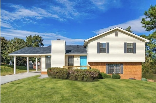 back of house featuring concrete driveway, a chimney, brick siding, a carport, and a lawn