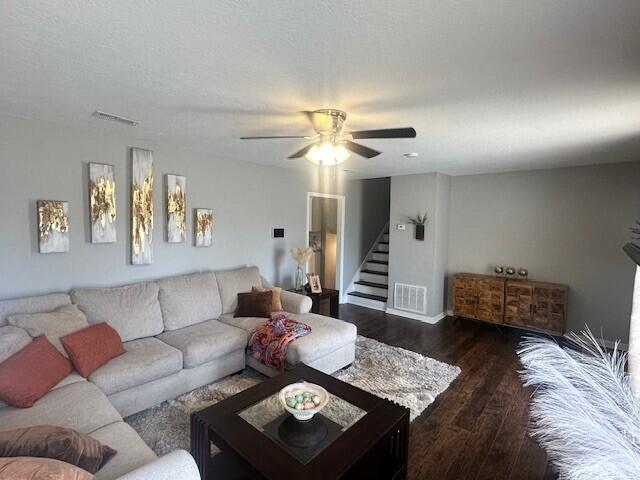 living room with dark wood-style floors, visible vents, stairway, and a ceiling fan