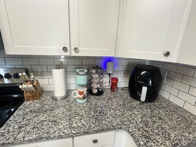 room details with decorative backsplash, white cabinets, stone countertops, and electric range