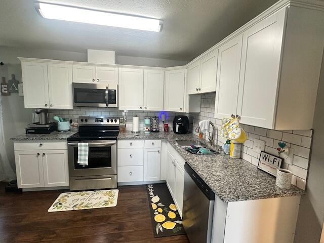 kitchen featuring light stone counters, a sink, white cabinetry, appliances with stainless steel finishes, and dark wood-type flooring