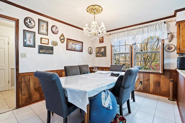 dining space featuring light tile patterned floors, wooden walls, wainscoting, an inviting chandelier, and crown molding