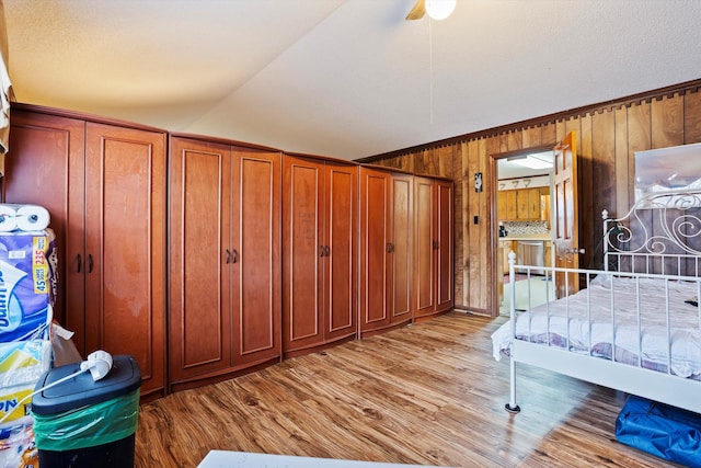 bedroom with light wood finished floors, wooden walls, lofted ceiling, ceiling fan, and ornamental molding