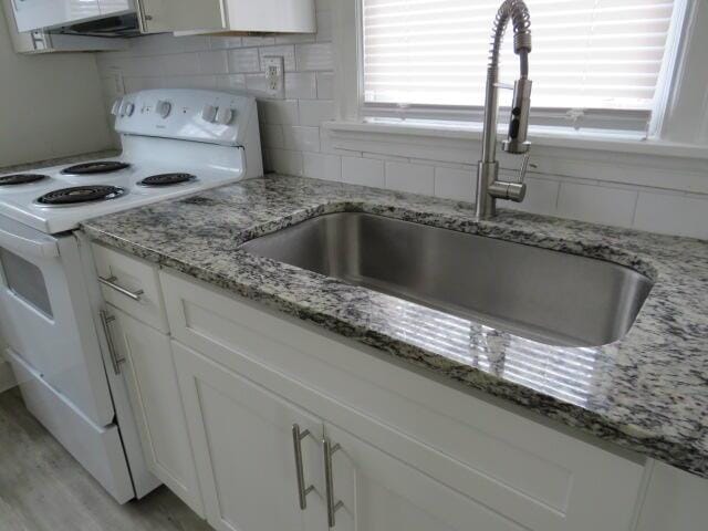 kitchen featuring light stone countertops, sink, tasteful backsplash, white range with electric cooktop, and white cabinets