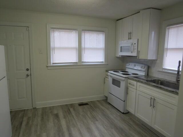 kitchen with dark stone counters, white appliances, sink, light hardwood / wood-style flooring, and white cabinets