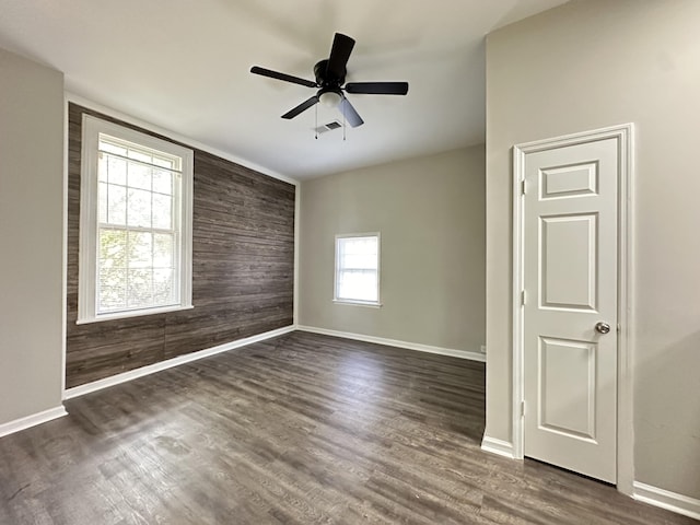 empty room with dark hardwood / wood-style flooring, a wealth of natural light, wooden walls, and ceiling fan