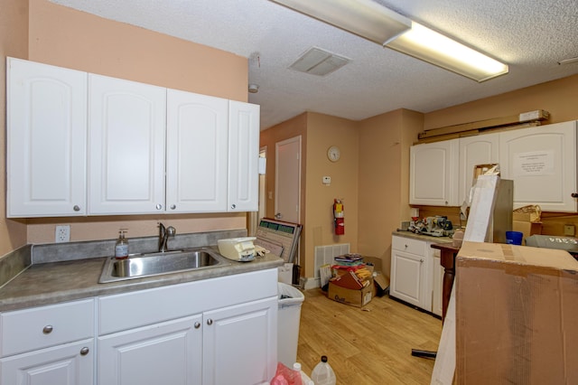 kitchen featuring sink, white cabinets, light hardwood / wood-style floors, and a textured ceiling