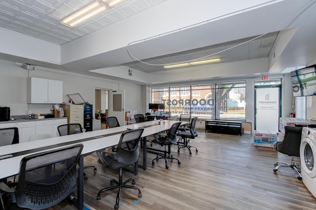 home office with a tray ceiling, light hardwood / wood-style flooring, and washer / dryer