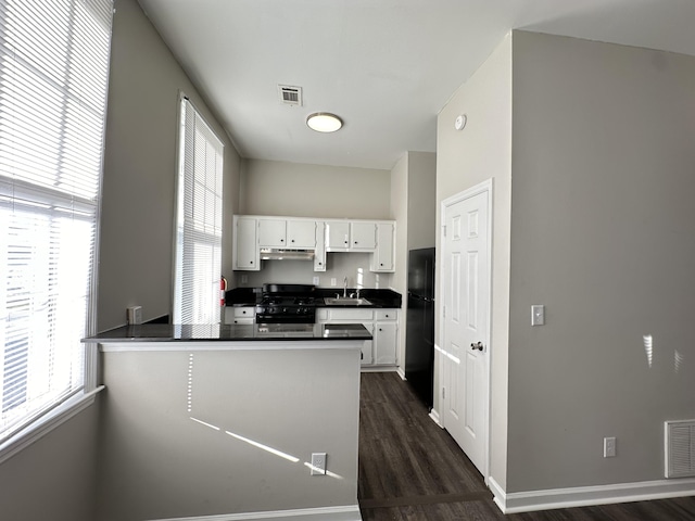 kitchen with kitchen peninsula, black refrigerator, white cabinets, dark hardwood / wood-style floors, and stainless steel range with gas stovetop