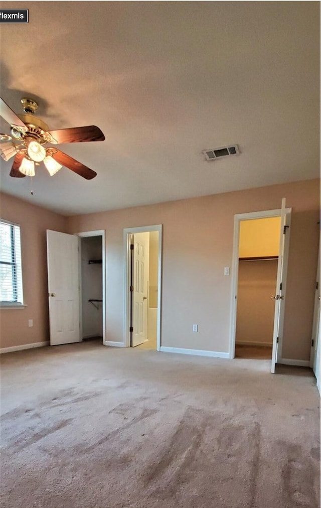 unfurnished bedroom with a walk in closet, light colored carpet, and ceiling fan