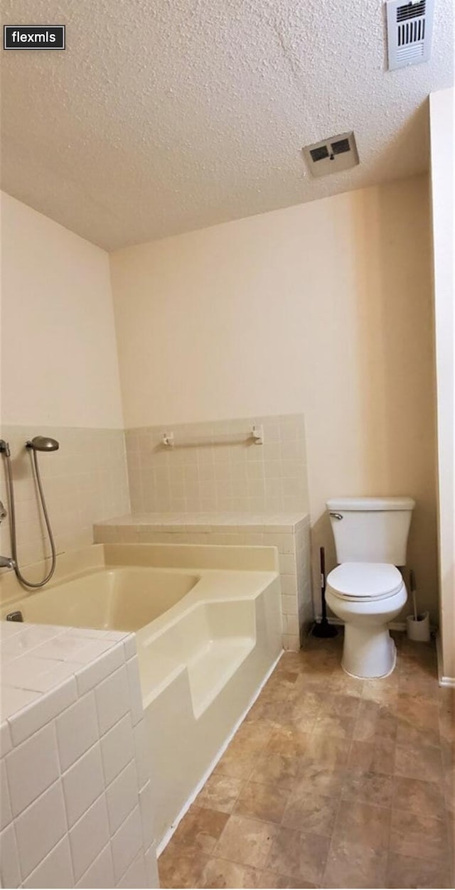 bathroom with a washtub, toilet, and a textured ceiling