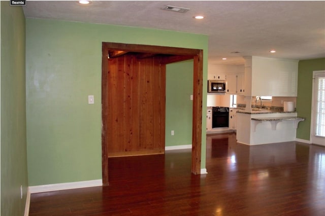 kitchen featuring white cabinets, sink, light stone counters, black oven, and dark hardwood / wood-style flooring