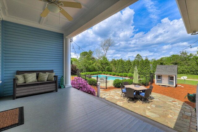 deck with a shed, a ceiling fan, an outdoor structure, outdoor dining space, and a fenced in pool