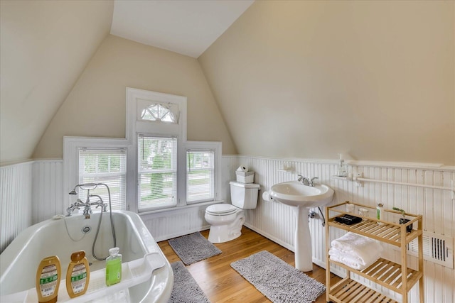 full bathroom featuring a wainscoted wall, toilet, wood finished floors, lofted ceiling, and a bathtub
