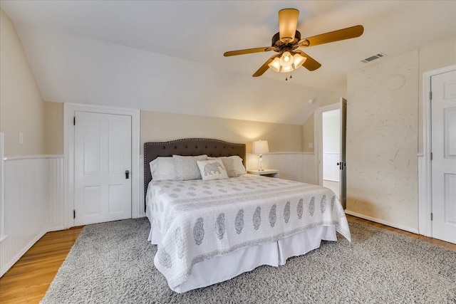 bedroom with light wood-style floors, visible vents, lofted ceiling, and a wainscoted wall