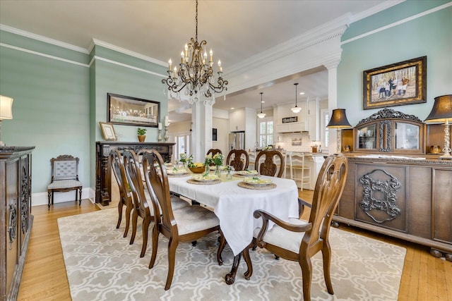 dining area featuring crown molding, ornate columns, a chandelier, light wood finished floors, and baseboards