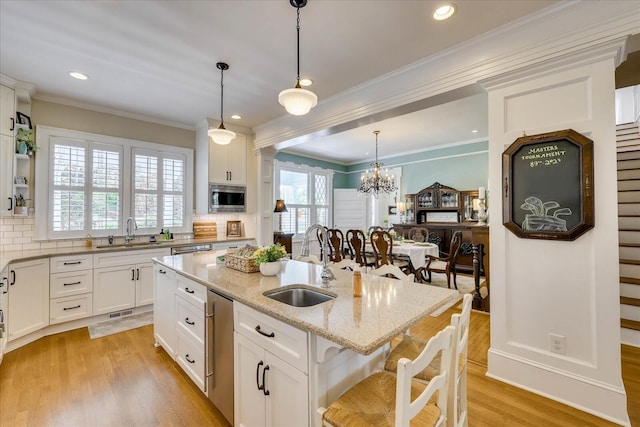 kitchen featuring a sink, backsplash, stainless steel microwave, and white cabinets