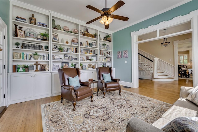 sitting room with ornamental molding, ceiling fan, stairway, and light wood-style floors