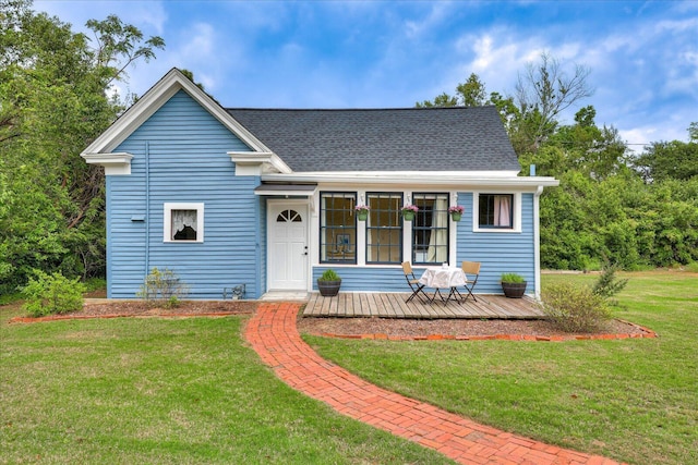 view of front of home featuring a front yard, a deck, and a shingled roof