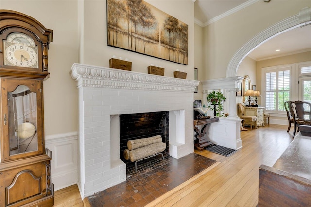 living area with arched walkways, a fireplace, hardwood / wood-style floors, and crown molding