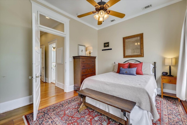 bedroom with ornamental molding, visible vents, baseboards, and wood finished floors