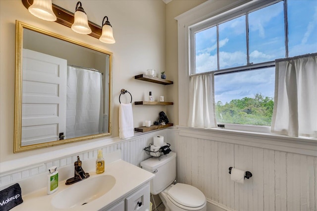 full bath featuring vanity, a shower with curtain, toilet, wood walls, and wainscoting