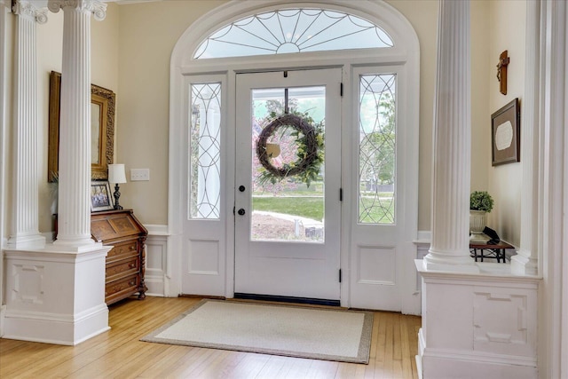 foyer entrance featuring a decorative wall, light wood-style flooring, ornate columns, and a wainscoted wall