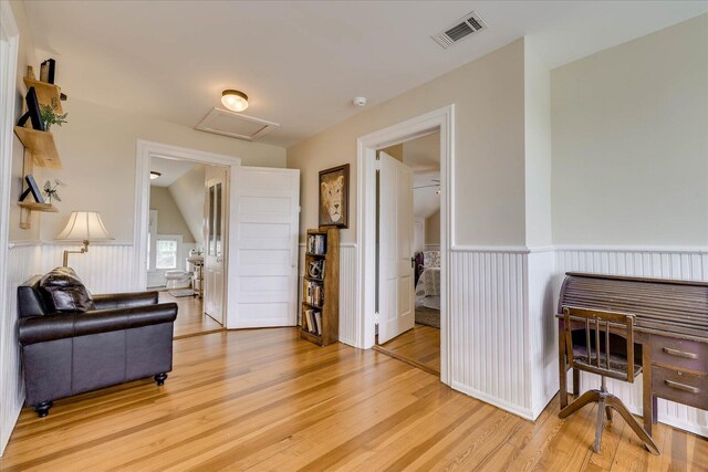 living area with light wood finished floors, attic access, visible vents, and a wainscoted wall