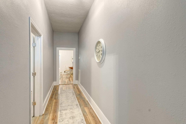 hall with a textured ceiling and light hardwood / wood-style flooring