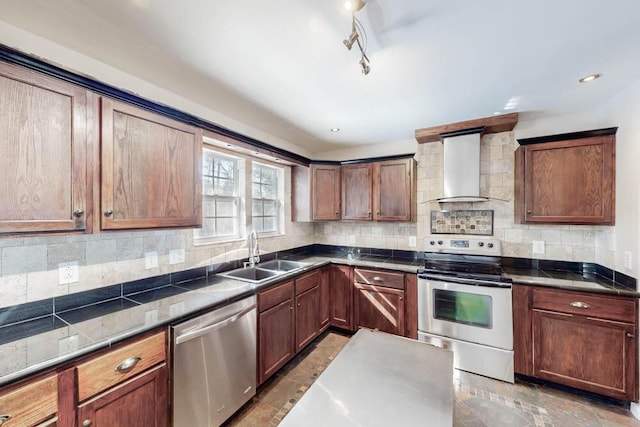 kitchen featuring rail lighting, sink, decorative backsplash, stainless steel appliances, and wall chimney range hood