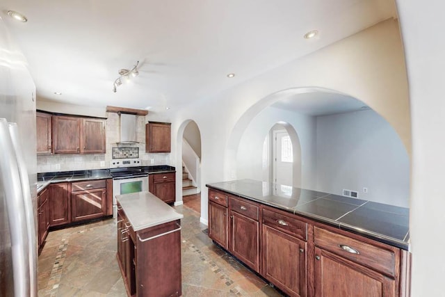 kitchen featuring stainless steel appliances, tasteful backsplash, a center island, and wall chimney exhaust hood