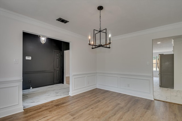 unfurnished dining area featuring a chandelier, ornamental molding, a decorative wall, wood finished floors, and wainscoting