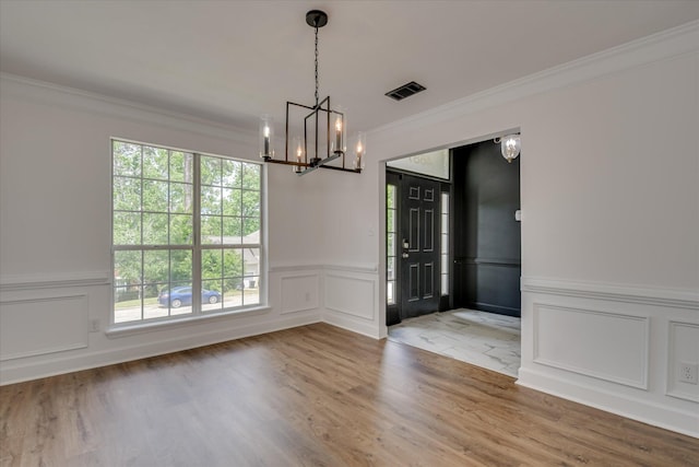 unfurnished dining area with a decorative wall, a chandelier, ornamental molding, wood finished floors, and a wainscoted wall