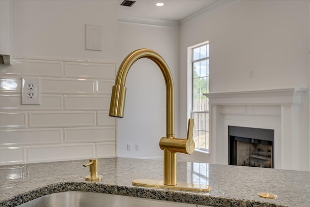kitchen view of stone counters, a sink, a fireplace, white cabinets, and ornamental molding