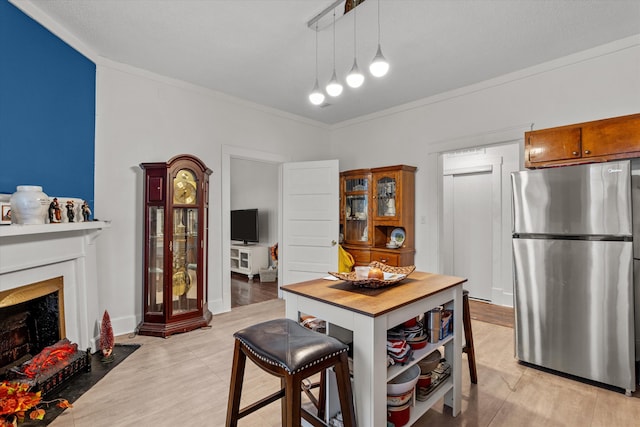 kitchen with stainless steel refrigerator, ornamental molding, decorative light fixtures, and light wood-type flooring